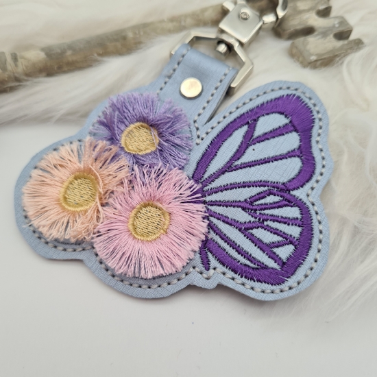 Taschenanhänger / Taschenbaumler Schmetterling mit Blumen grau/lila